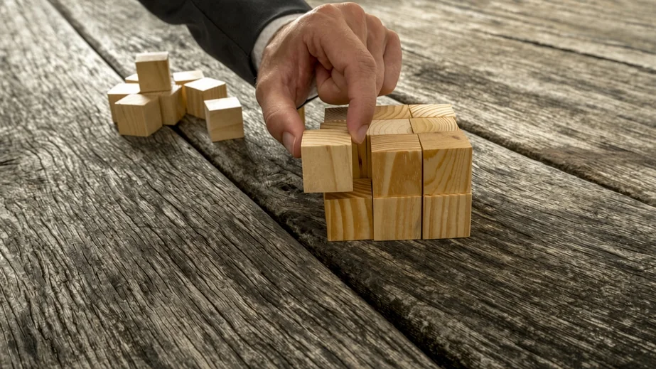 A hand placing wooden blocks, a symbol of building a business step by step.